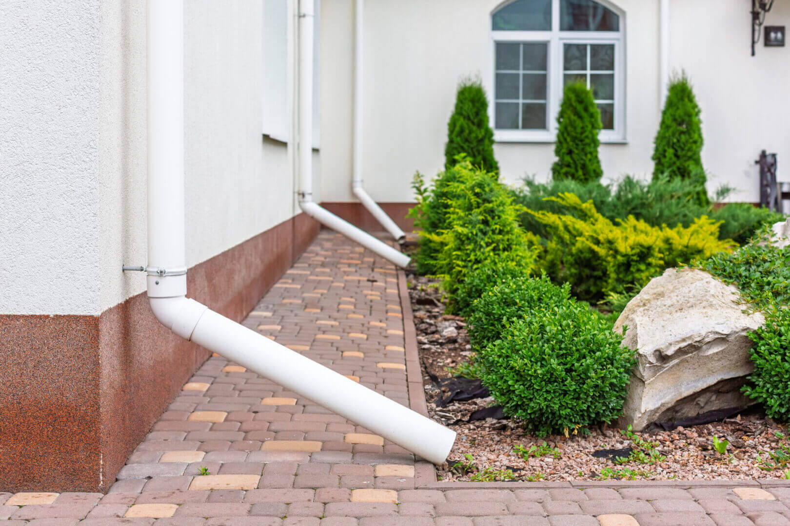 White downspouts directing rainwater away from a house foundation.