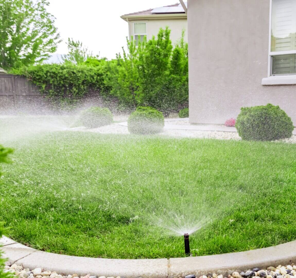 A lawn sprinkler watering a green garden near a house.