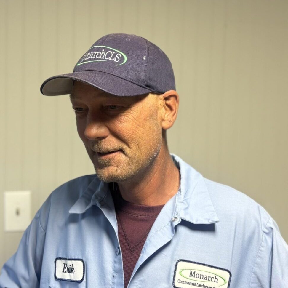 A man in a blue work shirt and cap smiles gently indoors.