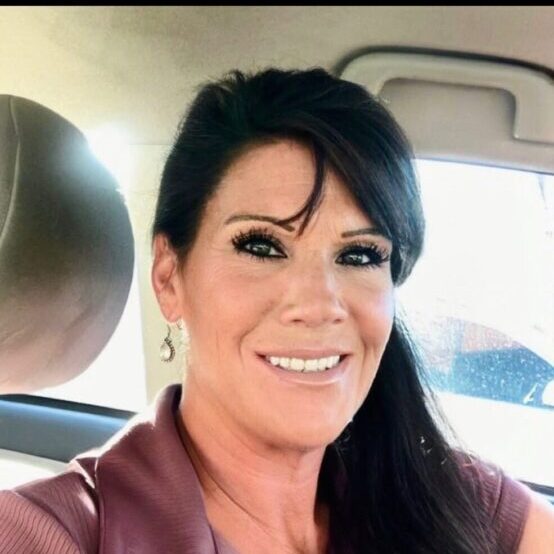 Woman smiling in car, wearing purple shirt.